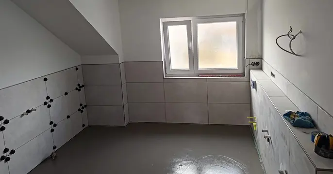Helle Wandfliesen unter einer Dachschräge während der Verlegung, mit Nivellierhilfen